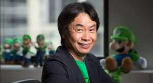 Shigeru Miyamoto smiling at Nintendo with Luigi plush toys behind him