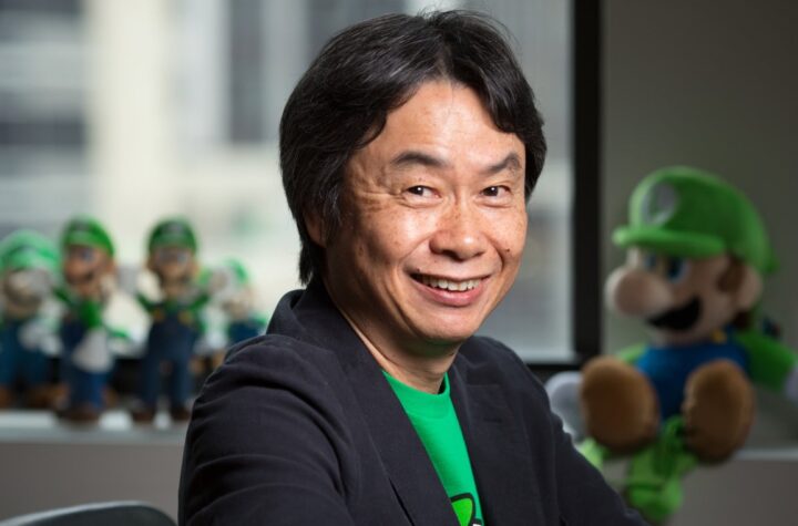 Shigeru Miyamoto smiling at Nintendo with Luigi plush toys behind him